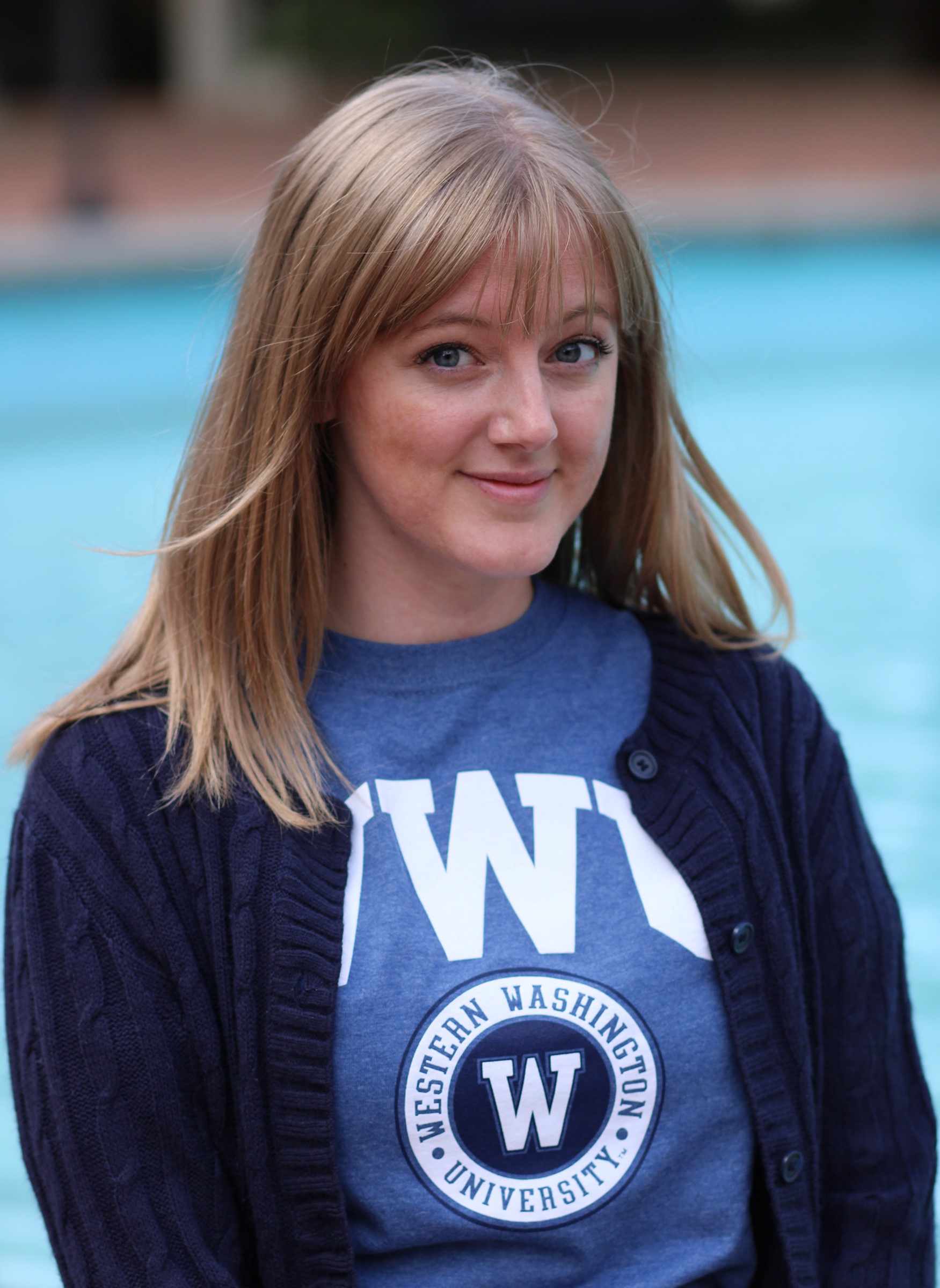 Breezy smiling, wearing blue "WWU" shirt and dark sweater, standing in front of light blue fountain