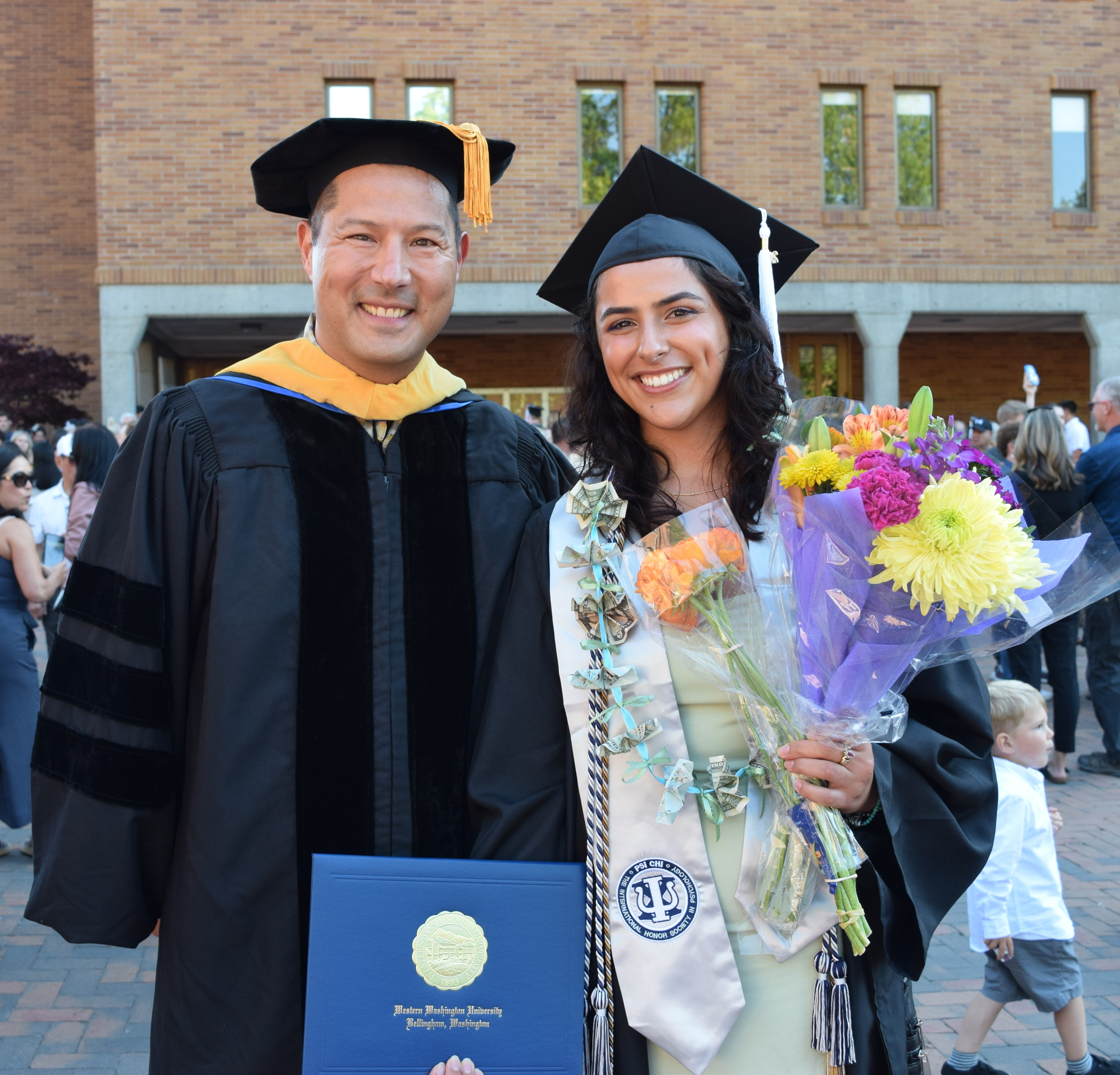 Jasmine and Dr. Czopp smiling wearing graduation regalia and holding flowers