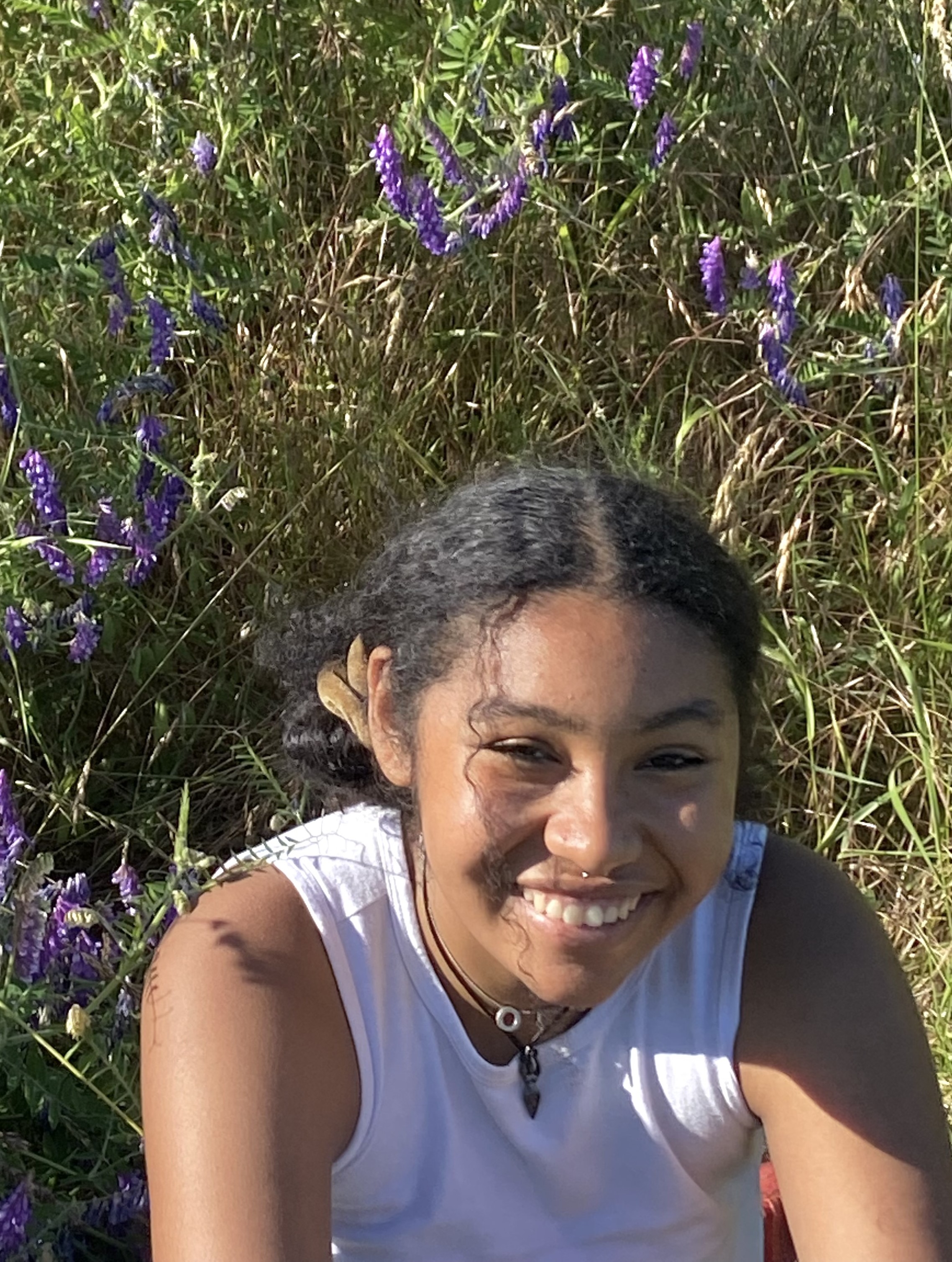 Sophia smiling, wearing a white tank top and sitting in a field of lavender 